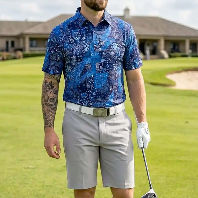 Man in a blue patterned shirt and gray shorts holding a golf club on a golf course.