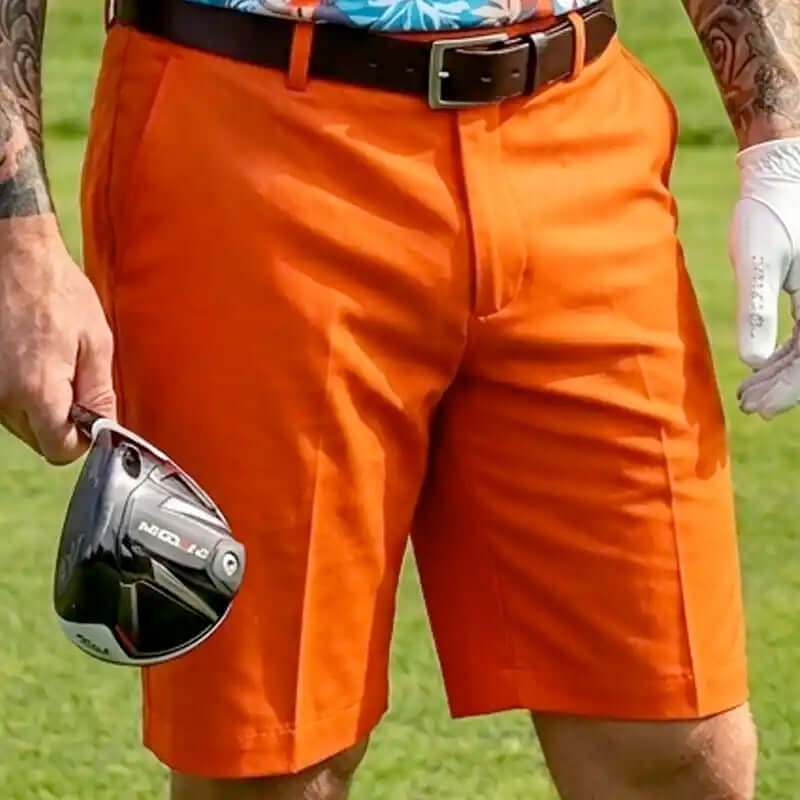golfer wearing orange golf shorts holding a golf club on a grassy field