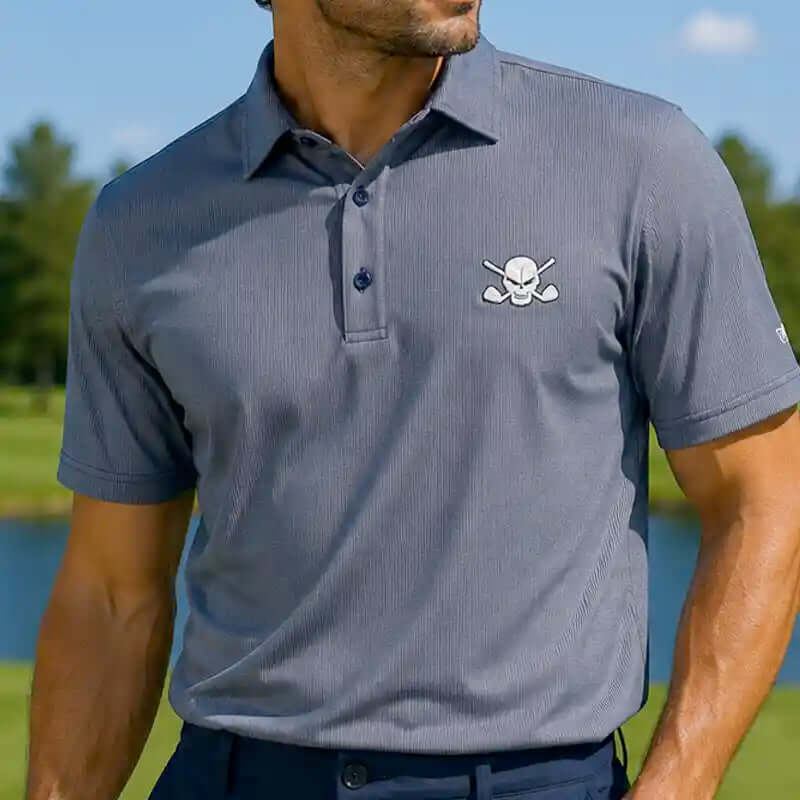 Man wearing a gray polo shirt with a skull and crossbones design on a golf course.