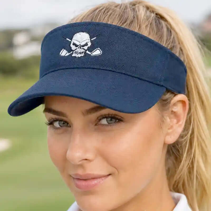 A woman wearing a navy blue golf visor with a white embroidered skull and crossed clubs logo that reads 'RUMI'. The background is a blurred outdoor golf course.