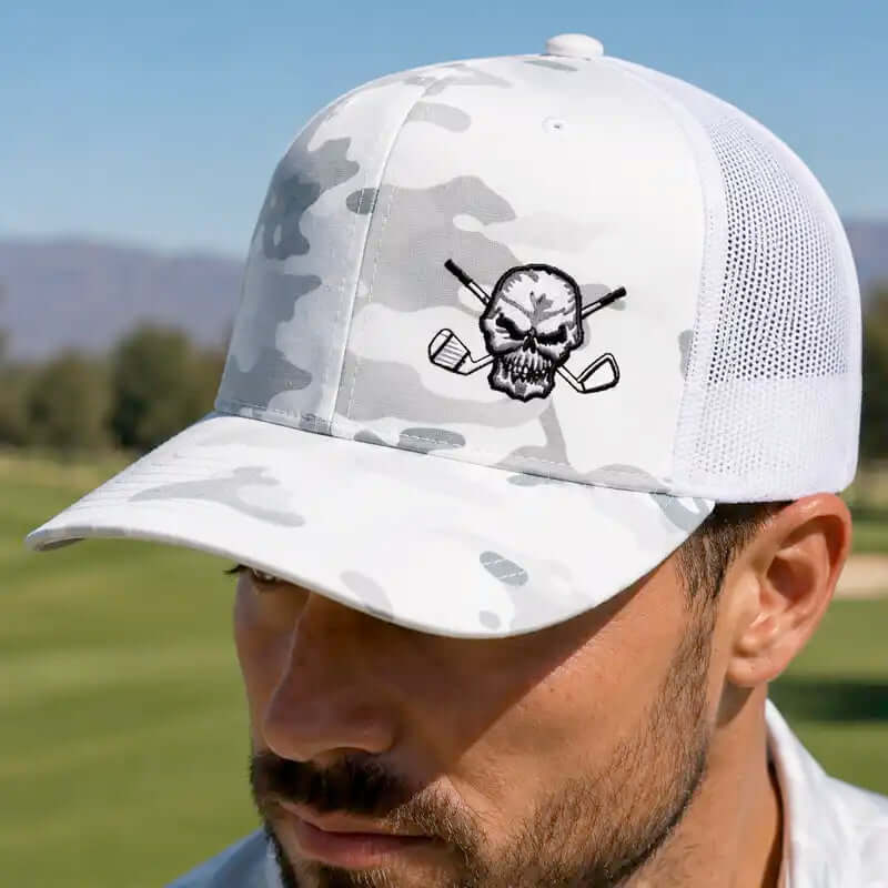 A man wearing a white and gray camouflage trucker golf hat with a black embroidered skull and golf clubs logo on the front.