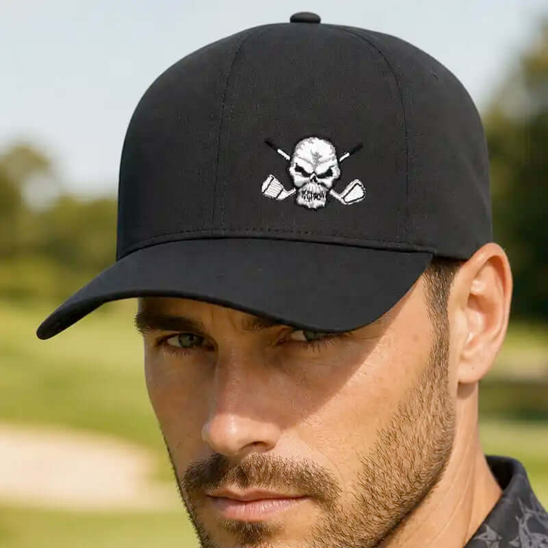 A man wearing a black baseball hat with a white embroidered skull and crossed golf clubs logo, set against a blurred golf course background.