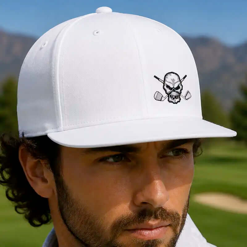 A man wearing a white flat brim golf hat with a black embroidered skull and crossed golf clubs logo