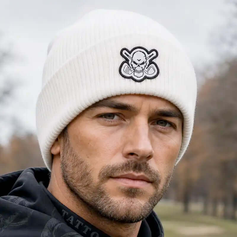 A man wearing a white ribbed knit beanie with a black and white skull-and-crossbones style embroidered patch on the front