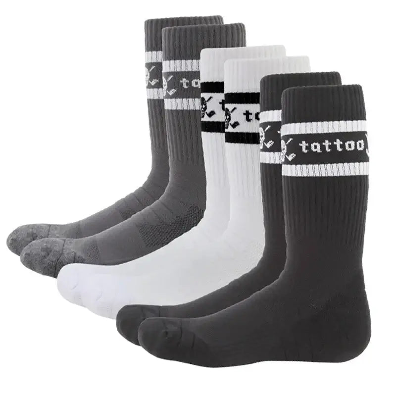 Three pairs of crew-cut golf socks, two in black and one in white, all featuring a skull and crossed clubs logo on the instep and the word 'tattoo' on the back.