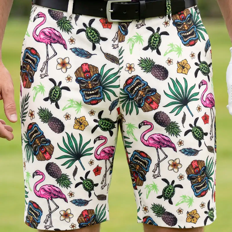 Close-up of Tiki golf shorts worn with a black belt, showing colorful tiki masks, pink flamingos and green turtles.