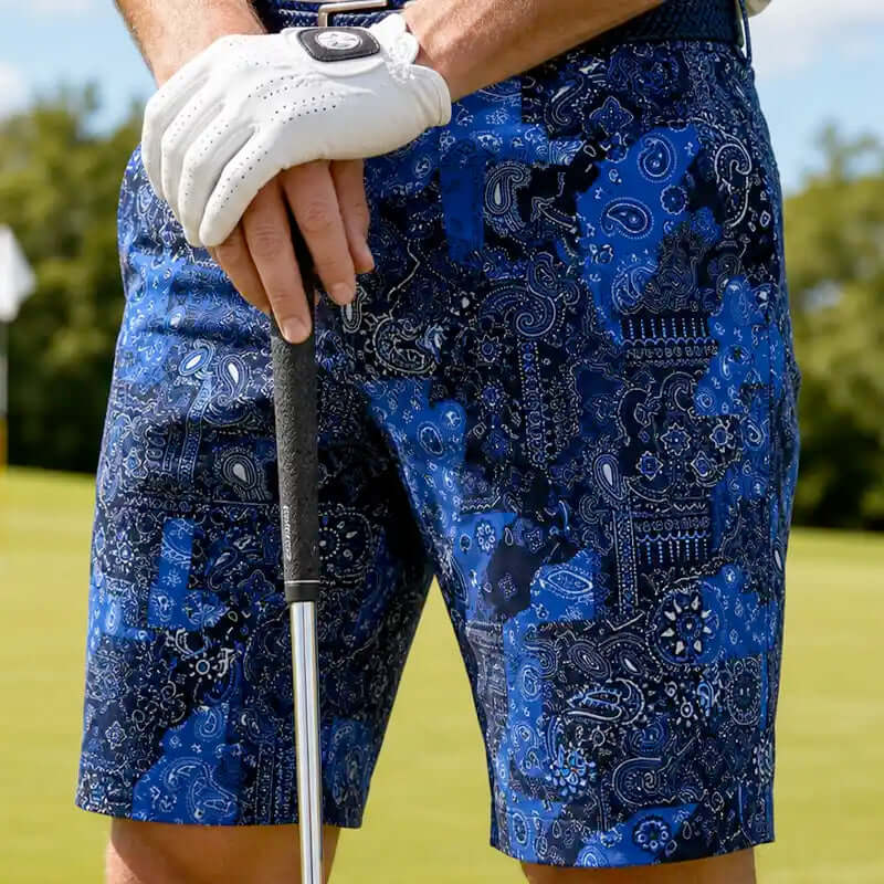 golfer wearing blue patterned golf shorts and a white golf glove holding a golf club on a golf course.