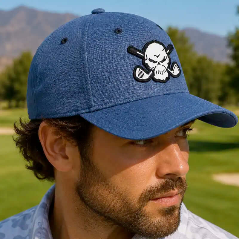 A man wearing a 1999 blue baseball cap with a white skull and crossed golf clubs patch on the front, photographed outdoors on a golf course.