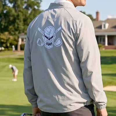golfer wearing a light gray jacket with a skull and golf clubs design on a golf course.