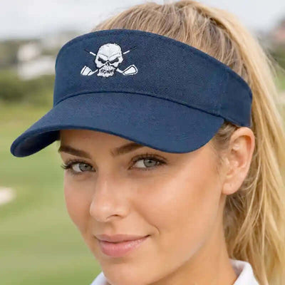 A woman wearing a navy blue golf visor with a white embroidered skull and crossed clubs logo that reads 'RUMI'. The background is a blurred outdoor golf course.