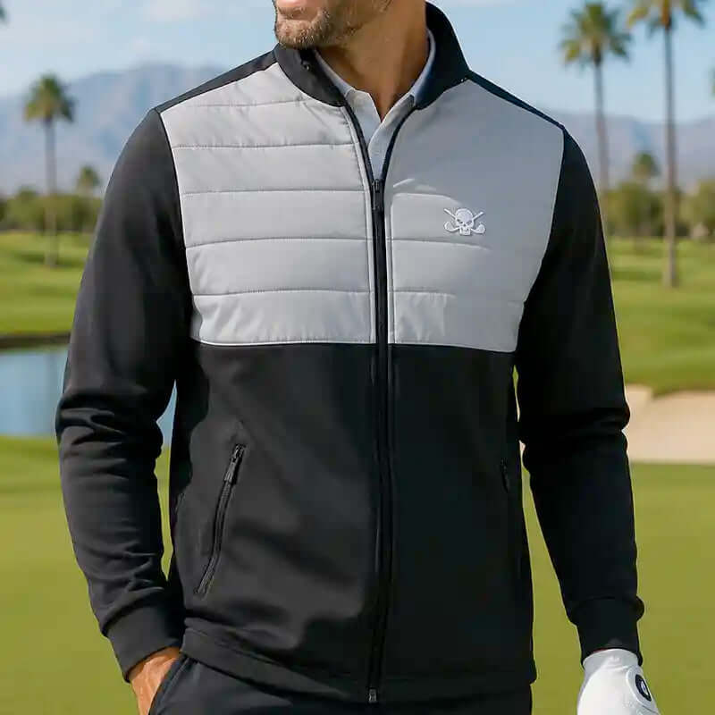 Man golfer wearing a black and gray jacket with a skull logo on a golf course.