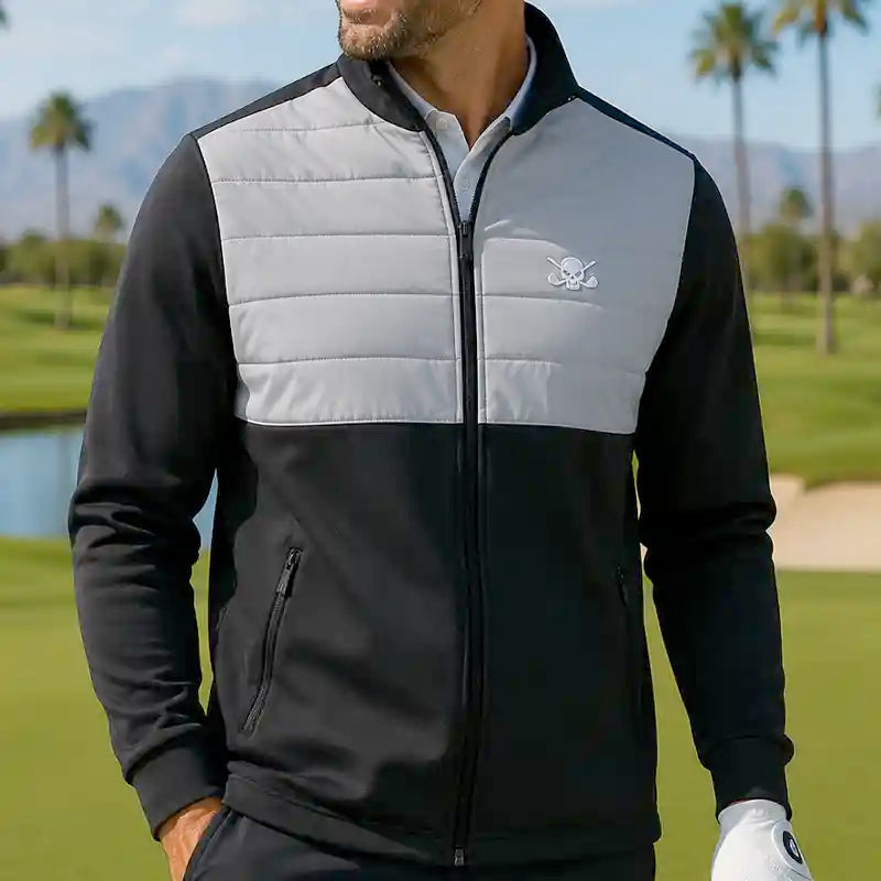 Man golfer wearing a black and gray jacket with a skull logo on a golf course.