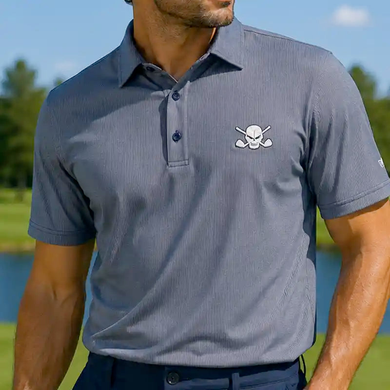 Man wearing a gray polo shirt with a skull and crossbones design on a golf course.
