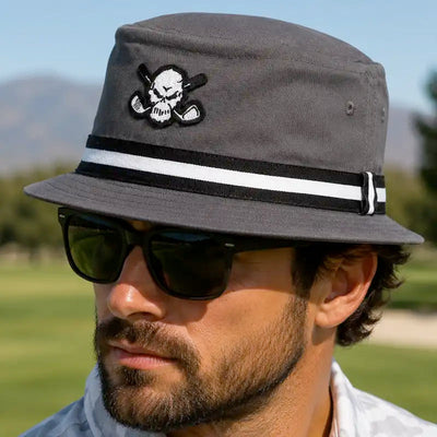 Man wearing a charcoal Tattoo Golf Premium Bucket golf hat with a skull patch and black-and-white striped band.