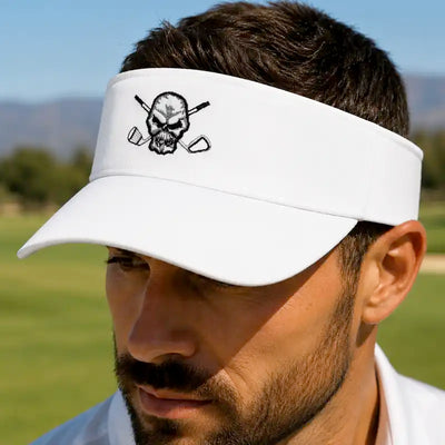 A golfer wearing a white golf visor with a black skull and crossed golf clubs logo, photographed outdoors on a golf course.