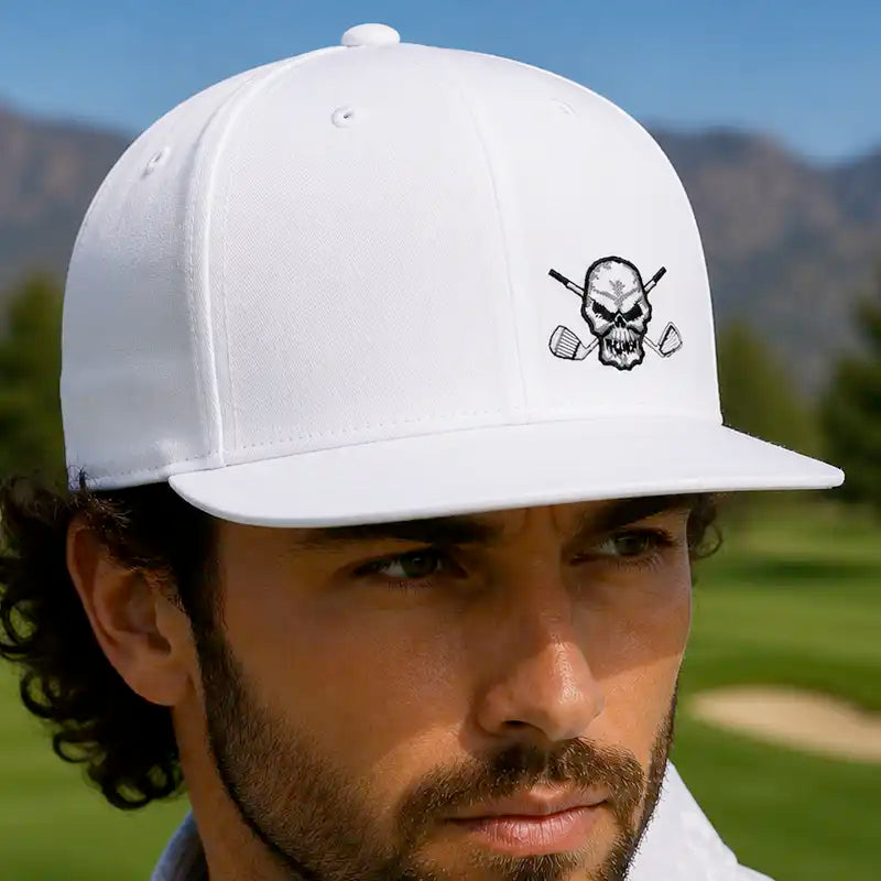 A man wearing a white flat brim golf hat with a black embroidered skull and crossed golf clubs logo
