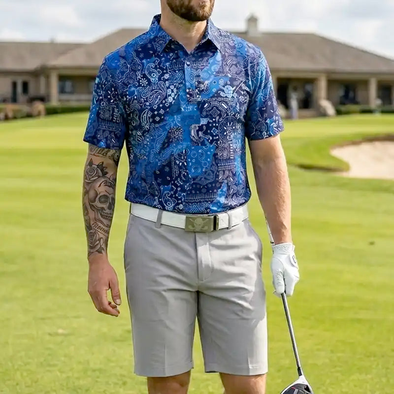 Man in a blue patterned shirt and gray shorts holding a golf club on a golf course.
