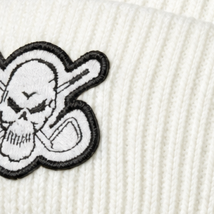 Close-up of a skull-and-crossed-clubs patch on a white rib-knit beanie.