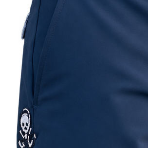 Close-up of navy shorts showing a side-pocket seam, patterned trim and small skull-and-crossed-clubs logo.