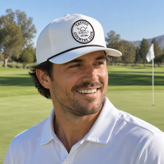 Smiling golfer wearing a white Tattoo Country Club cap and white polo.