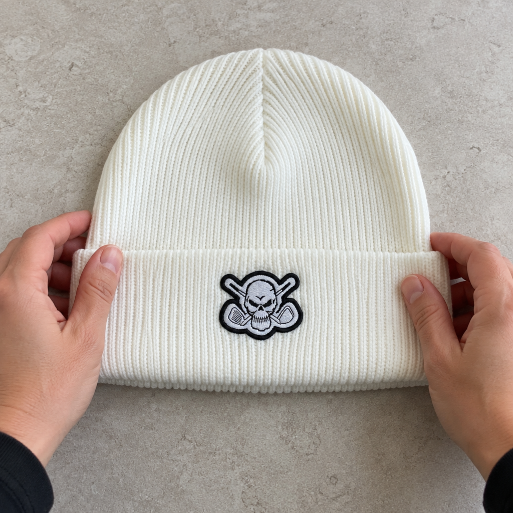 Hands holding a white skull-patch beanie flat on a pale surface.