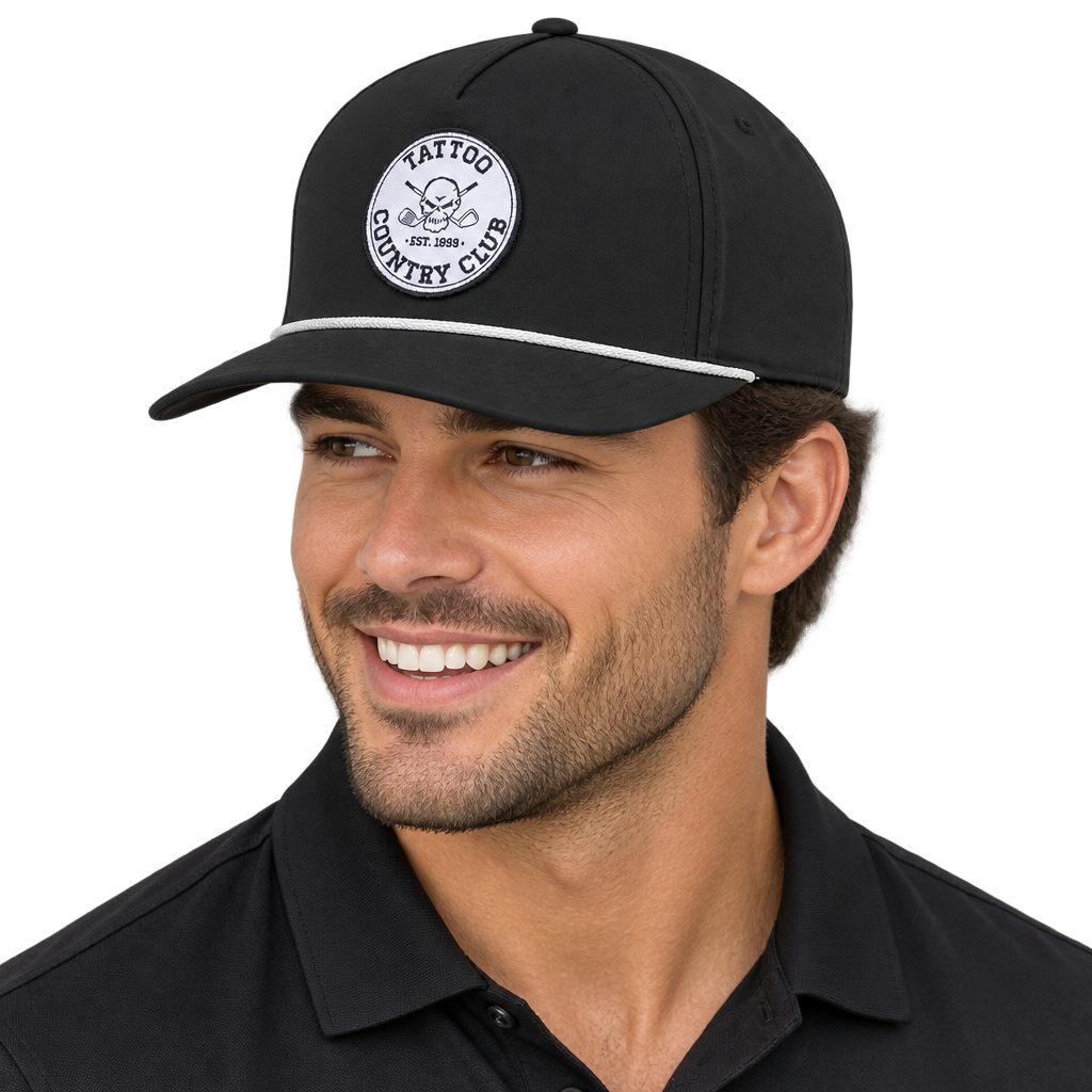 Man wearing a black Tattoo Country Club golf hat with a white circular skull patch and white rope trim.
