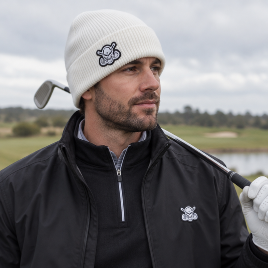 Golfer resting a club on his shoulder while wearing a white skull-patch beanie.