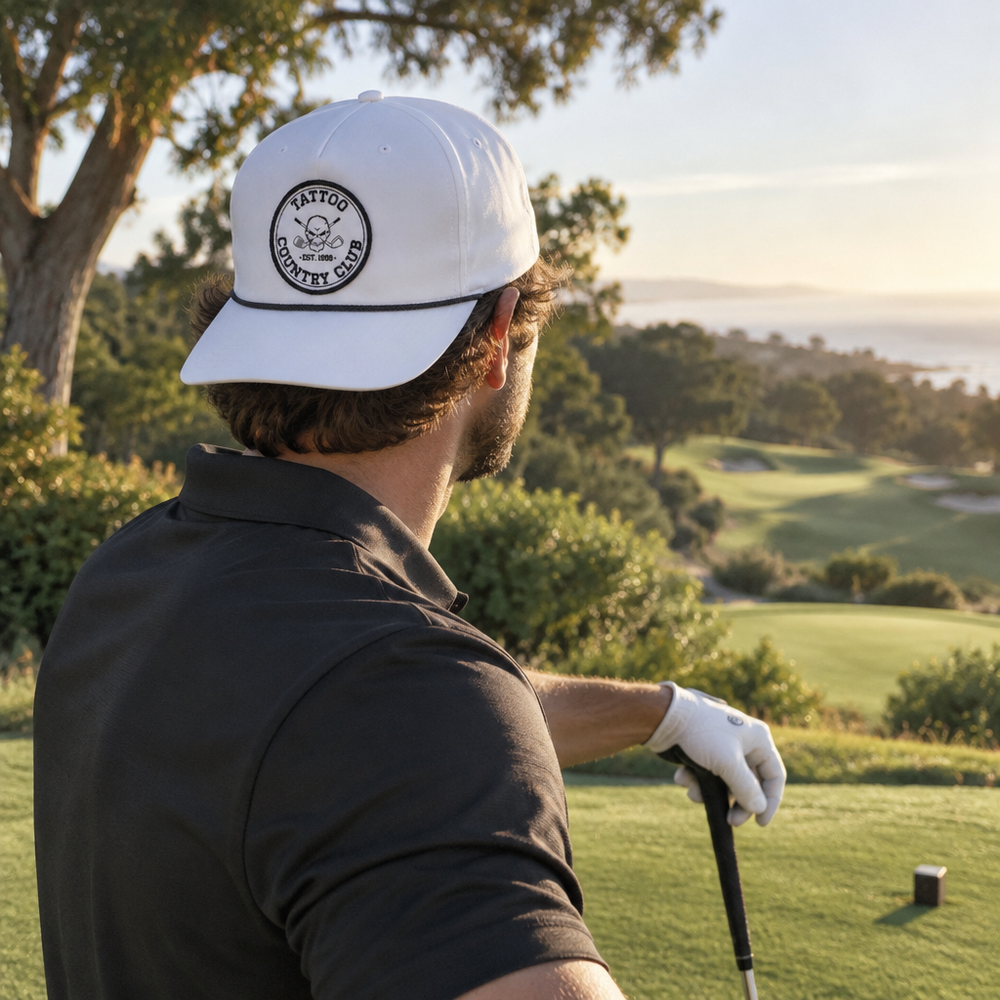 Golfer looking over a course while wearing a white cap backward, showing its circular skull patch.