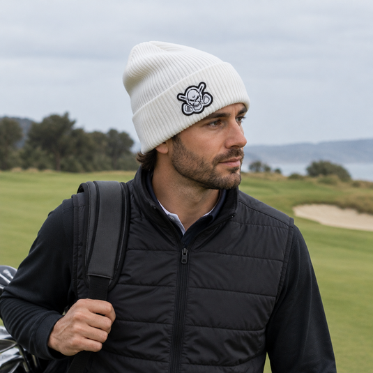 Golfer carrying a bag while wearing a white beanie and black padded vest.