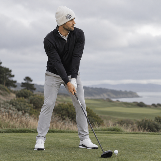 Golfer addressing a teed ball in a white beanie, black top and grey trousers.