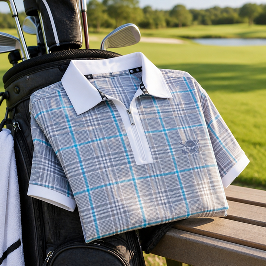 Folded grey and blue plaid golf polo resting beside a golf bag on an outdoor bench.