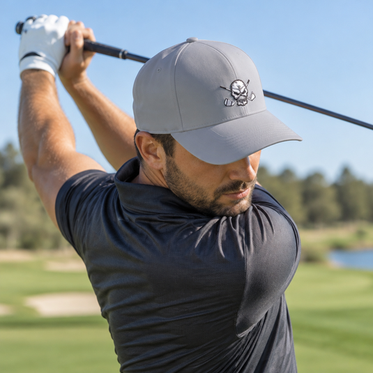Golfer raising a club behind his shoulders while wearing a grey skull-logo cap.