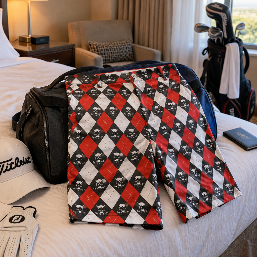 Red, white and black argyle golf shorts laid on a bed beside travel gear and a golf bag.