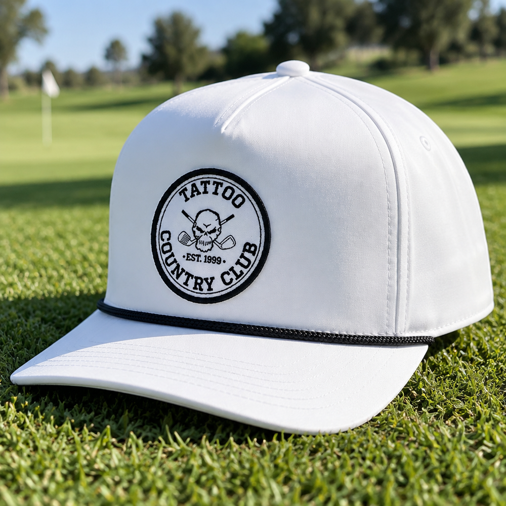 White Tattoo Country Club rope cap resting on grass.