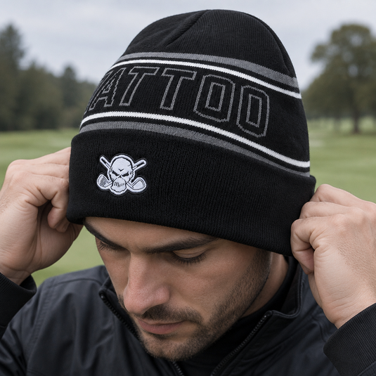 Golfer pulling a black TATTOO-lettered beanie down over his ears.