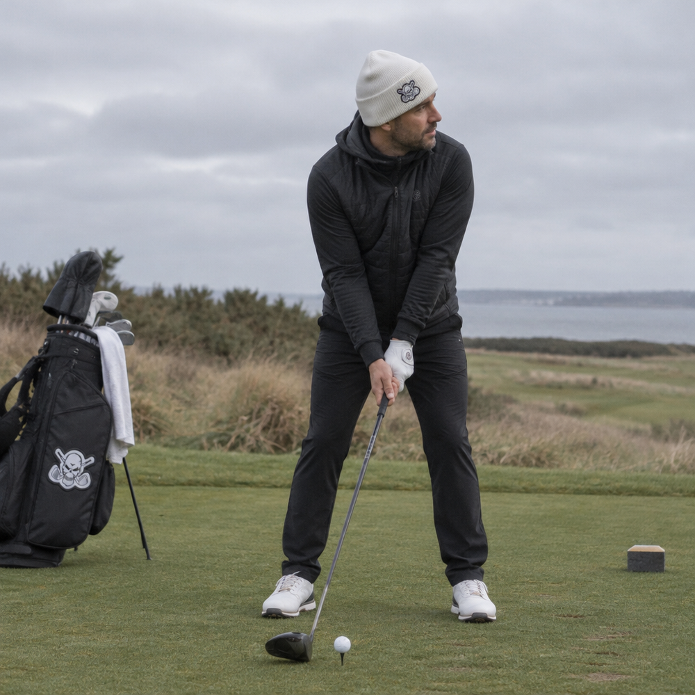 Golfer preparing a tee shot while wearing a white beanie and dark clothing.