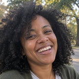 Portrait of a smiling woman with curly dark hair outdoors.