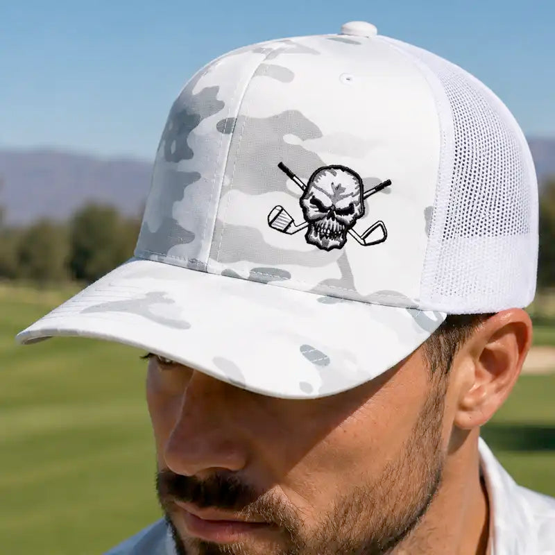 A man wearing a white and gray camouflage trucker golf hat with a black embroidered skull and golf clubs logo on the front.